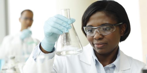 Female Researcher Examining Glass Beaker In Laboratory