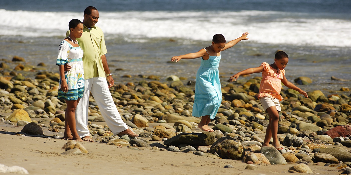 black mother, father, and two daughters walking along the seashore